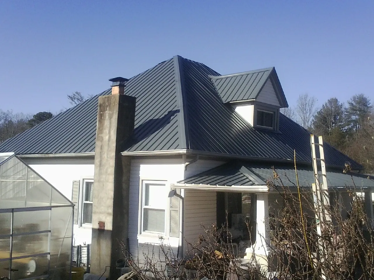 Dark blue standing seam metal roof on a white farmhouse with dormer — Slate & Tile Roof Repair by Roofing Brothers in Broadway