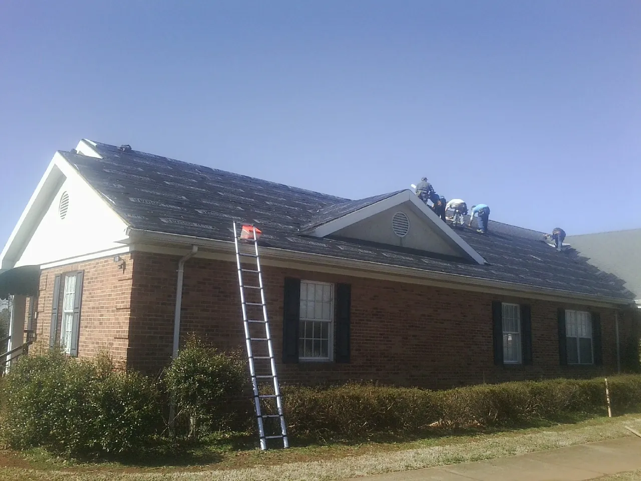 Crew tearing shingles off a brick ranch roof with a ladder set — Emergency Roof Repair work by our crew in Broadway