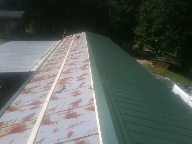 Old rusted panels beside newly installed green metal roofing — Wind Damage Roof Repair by Roofing Brothers in Broadway