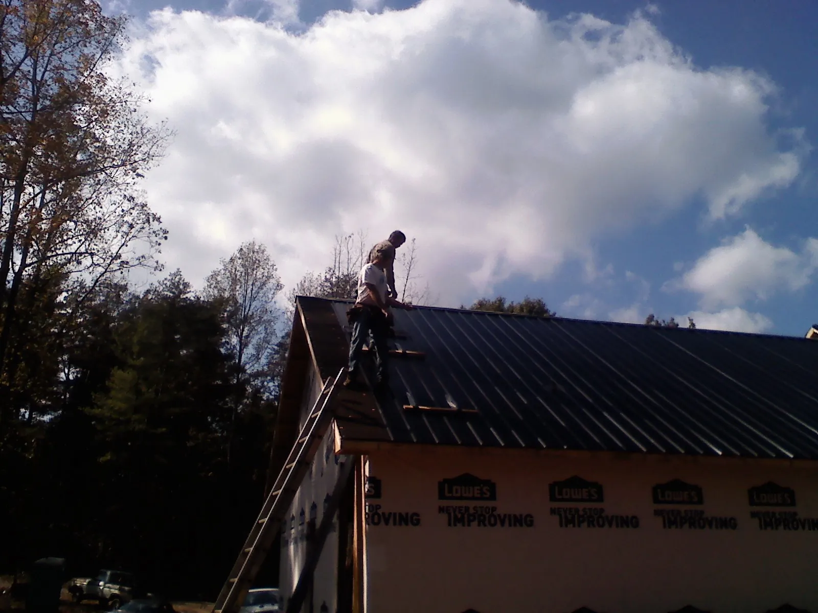 Roofer fastening dark metal panels high against a cloudy sky, from a Roof Inspection job in Broadway
